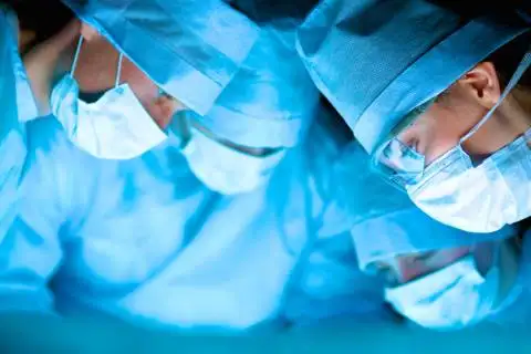 Surgical team in scrubs and masks performing a medical procedure in the operating room.