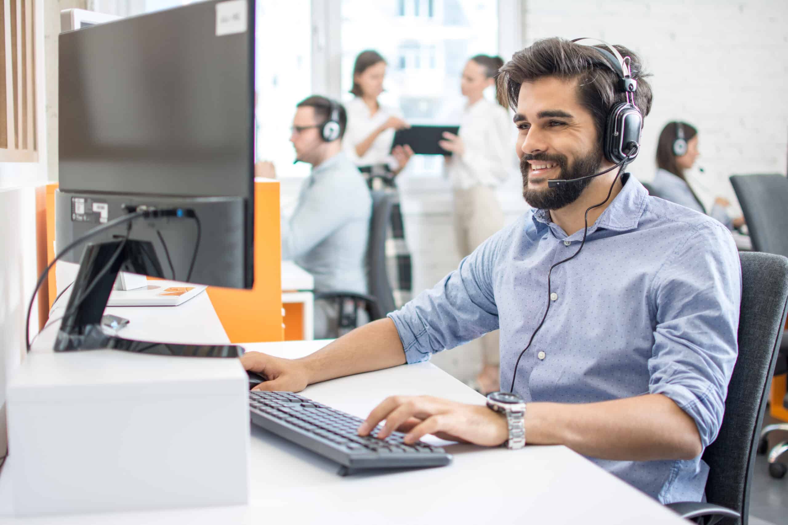 Support technician with headset providing IT assistance in a busy office environment.