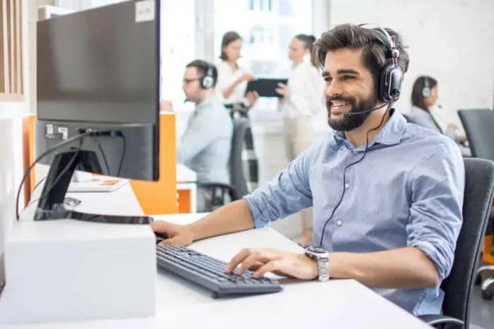 Support technician with headset providing IT assistance in a busy office environment.