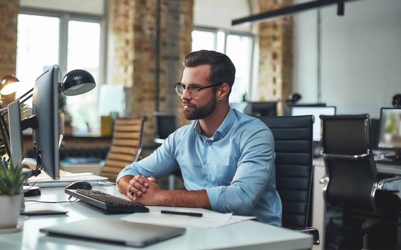 Side view of bearded man with glasses looking at computer monitor