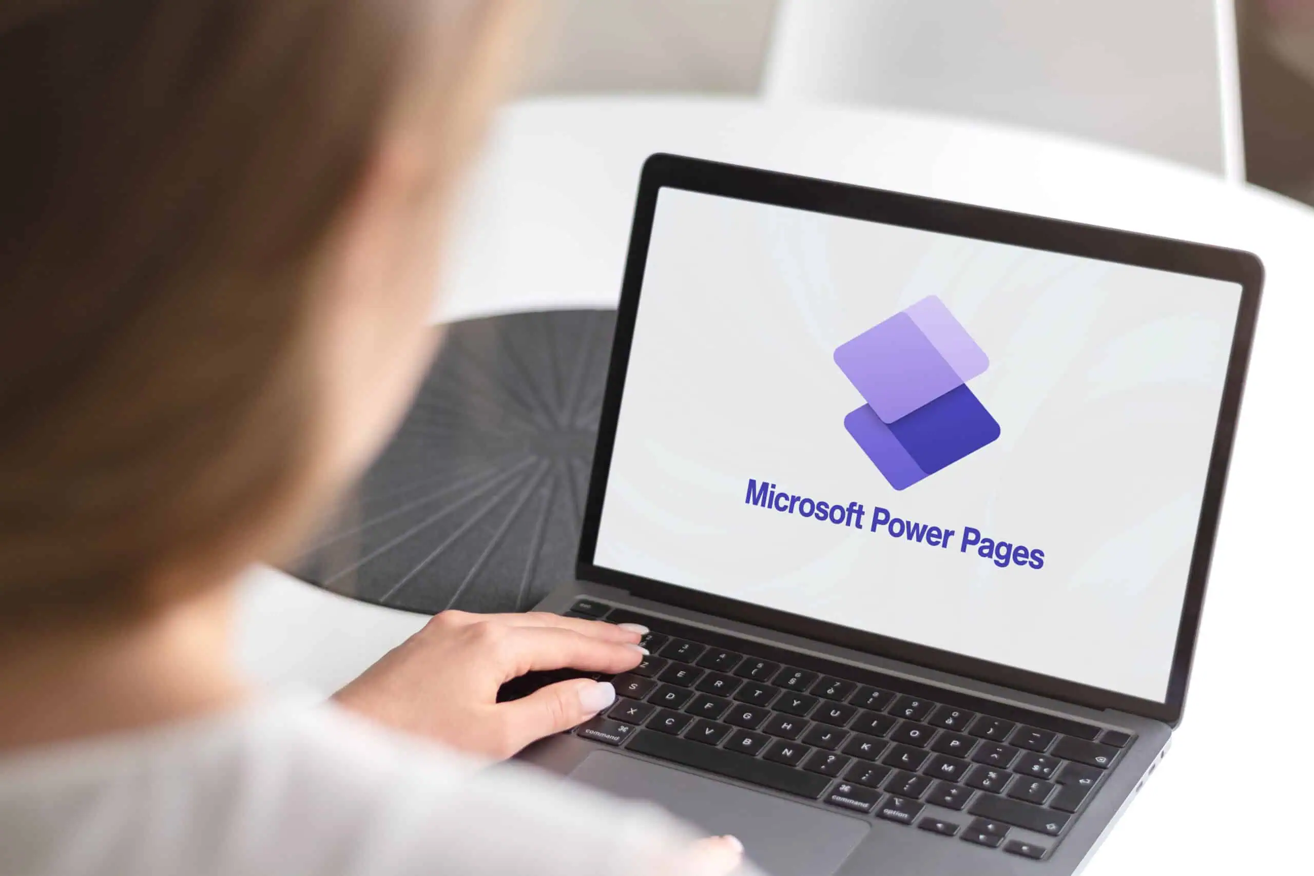 Microsoft Power Pages for Business Websites | i3solutions Person using a laptop displaying Microsoft Power Pages logo for website development.