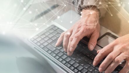 Hands typing on a laptop keyboard with digital network overlay.