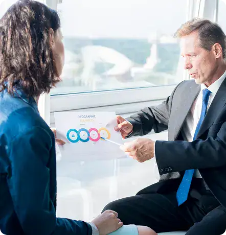 Business Meeting Discussing Data Presentation | i3solutions Two professionals in a meeting discuss an infographic report by a large window, with a man pointing at colorful charts.