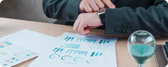 Dedicated Agile Teams Collaboration | i3solutions Businessperson in a dark suit examining printed charts and graphs on a desk beside a glass of water or liquid.