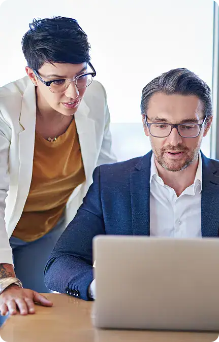 Professional Business Meeting with Laptop | i3solutions Two colleagues in an office looking at a laptop on a wooden table, collaborating closely.
