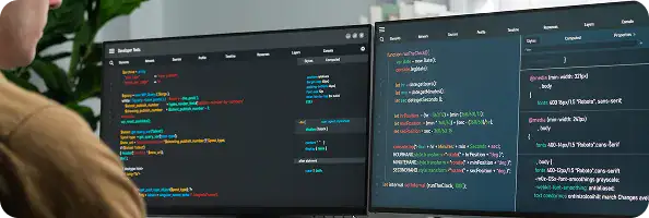 Software Developer Coding on Dual Monitors | i3solutions Person coding at a desk with two monitors displaying colorful code editors.