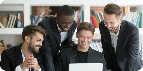 dotnet-architecture-led-delivery-teams Four colleagues gathered around a laptop, smiling as they collaborate in a bright office setting.