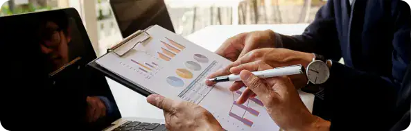 Business Collaboration and Data Analysis | i3solutions Two professionals review charts and graphs on a clipboard during a business meeting.Keep concise; avoid newlines though for screen readers.