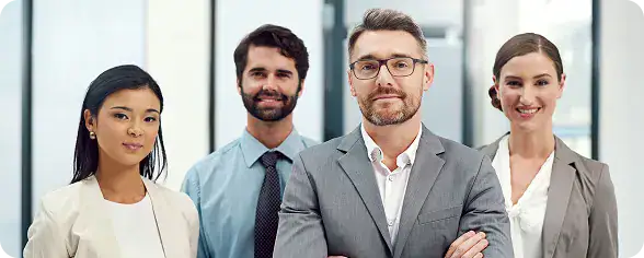 Professional Business Team for Azure Development | i3solutions Group of four professionals in business attire posing in a bright office lobby; two men and two women looking at the camera, front center man with glasses and folded arms.