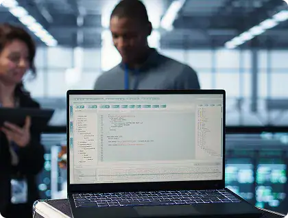 Software Development Team Collaboration | i3solutions Laptop with code editor on screen in a modern office; two colleagues blurred in the background.