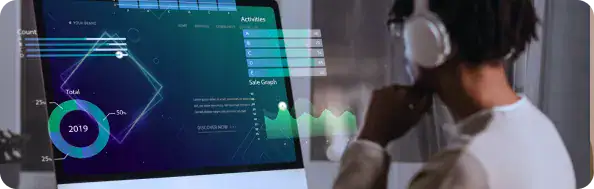Data Analytics Dashboard for Microsoft Fabric | i3solutions Person wearing headphones looks at a computer monitor displaying colorful charts and a translucent data dashboard overlay.