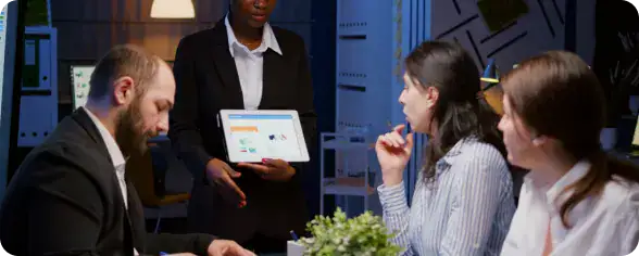 Dedicated Agile Teams Collaboration | i3solutions Businesswoman standing and presenting charts on a tablet to four colleagues in a conference room .