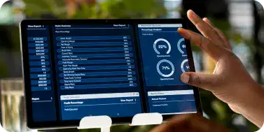Digital Dashboard for Data Monitoring | i3solutions A hand gestures toward two blue dashboard screens displaying charts and lists on a touchscreen setup.