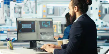 Advanced Manufacturing Technology Setup | i3solutions Bearded man in a suit working at a dual-monitor computer setup in a high-tech lab.