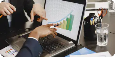 Business Meeting Analyzing Data | i3solutions Two businesspeople reviewing a laptop screen showing a colorful bar chart and line graph during a meeting.