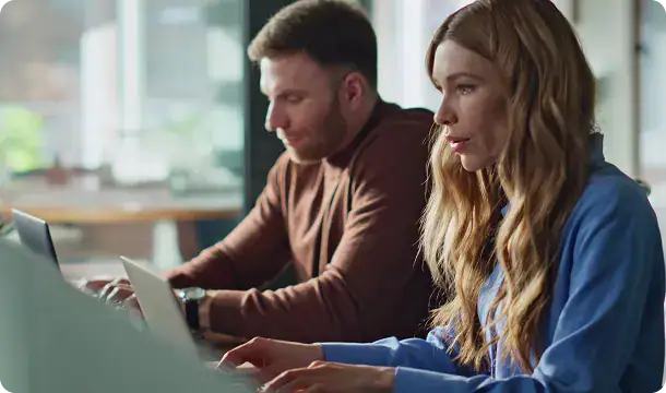 On-Demand Microsoft Experts Collaboration | i3solutions Two professionals working together on laptops in a modern office setting.