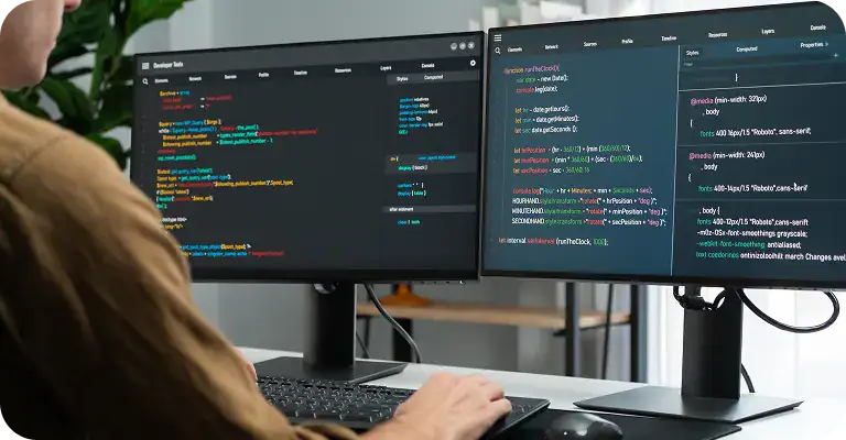 Person working on coding and system analysis on dual computer monitors.