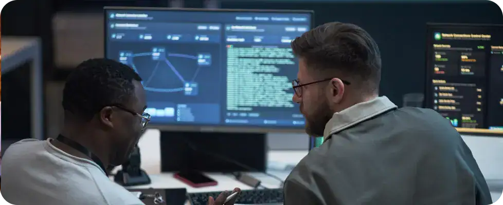 IT professionals analyzing data on monitors | i3solutions IT specialists working together with multiple screens displaying data and code.