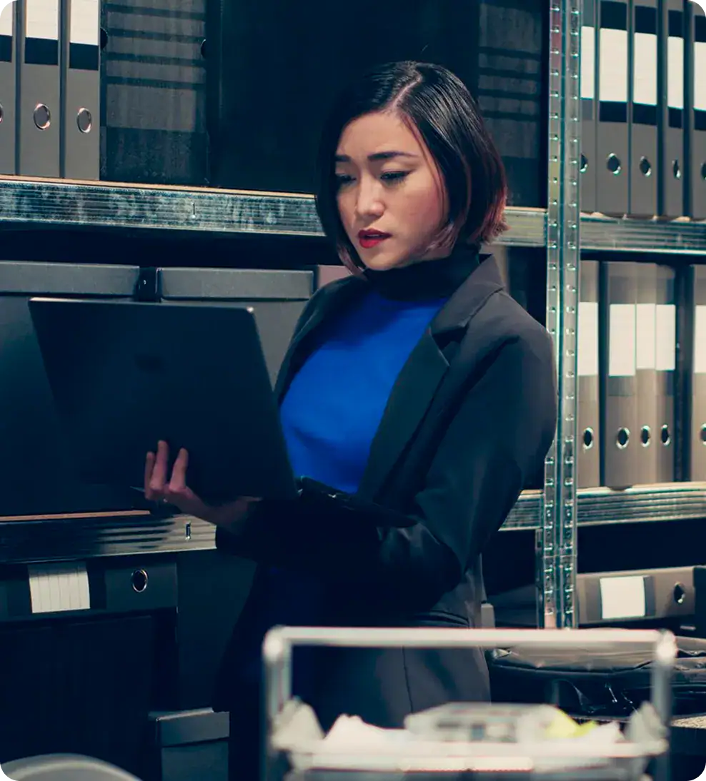 Businesswoman working on a laptop in a data storage room with shelves of binders.