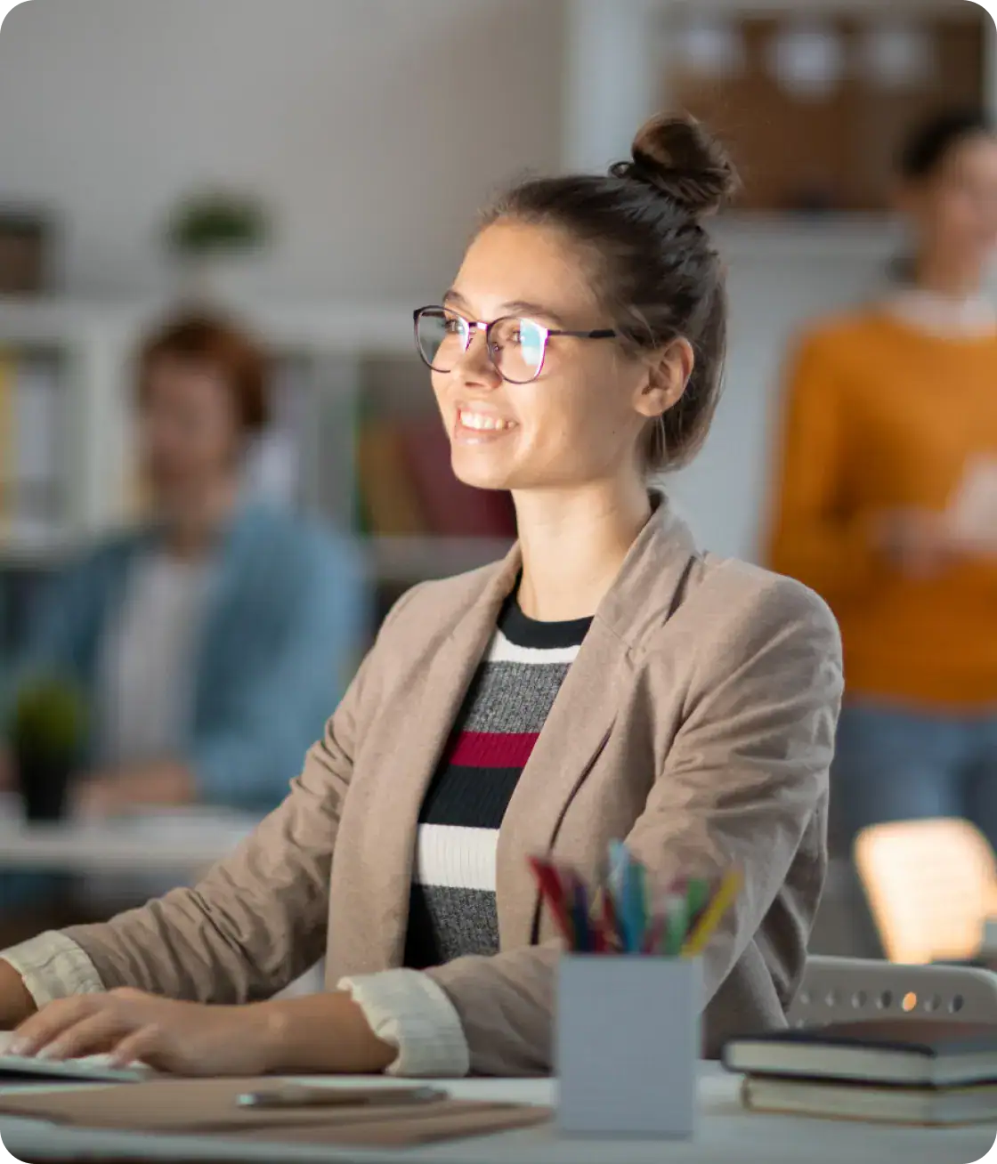 Young woman with glasses smiling at her desk in a modern office environment.
