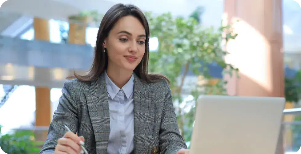 Businesswoman Analyzing Data on Laptop | i3solutions Businesswoman working on laptop in modern office with greenery.