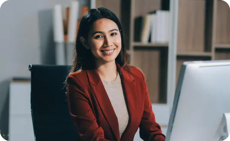 Smiling woman in business attire at her office desk with computer.