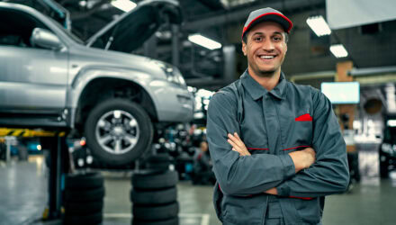 Automotive Technician Smiling in a Car Repair | i3solutions Automotive technician smiling in a car repair shop with a vehicle on a lift.