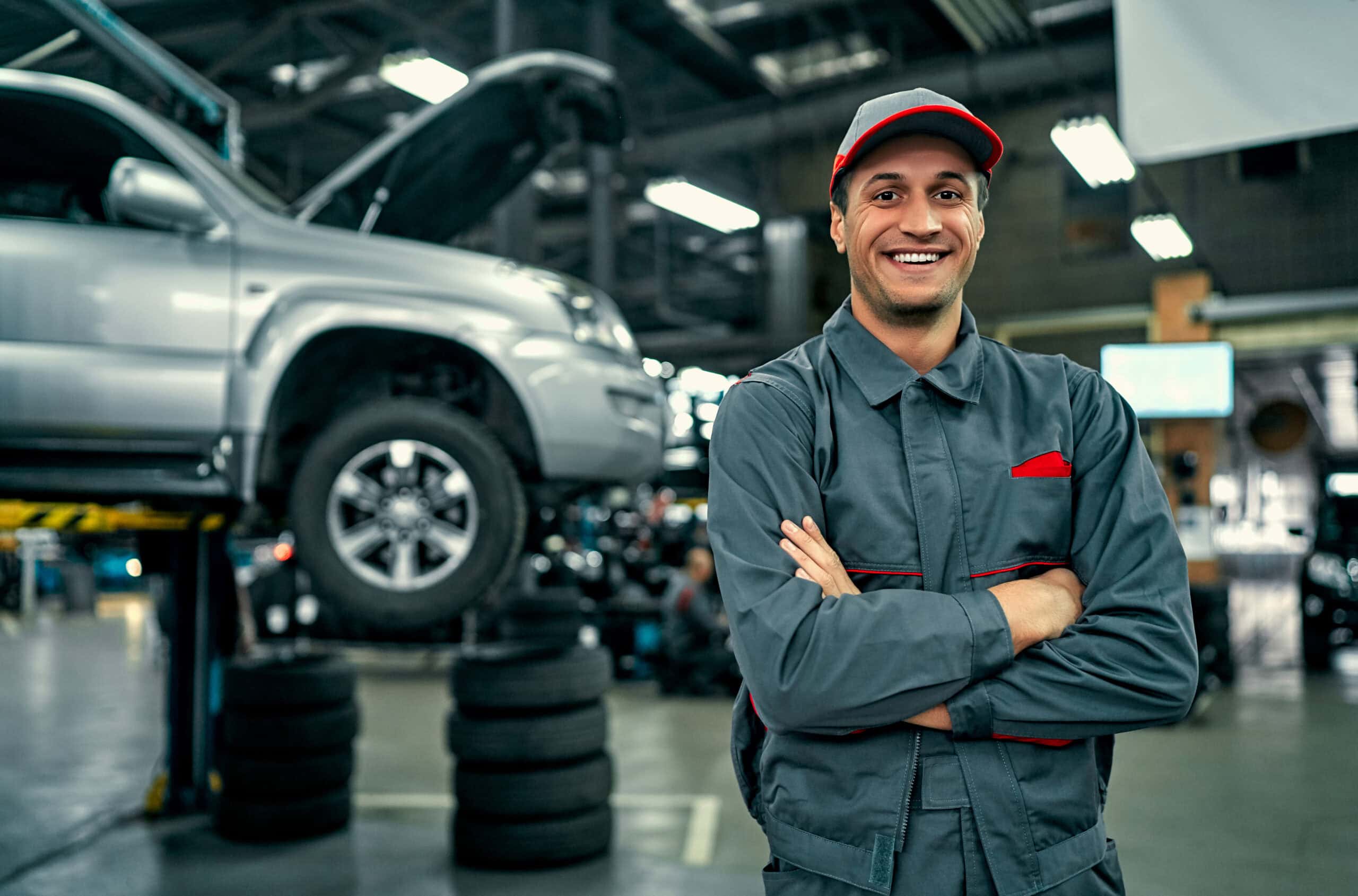 Automotive Technician Smiling in a Car Repair | i3solutions Automotive technician smiling in a car repair shop with a vehicle on a lift.