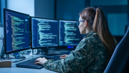 Female programmer coding on multiple monitors in a modern office.