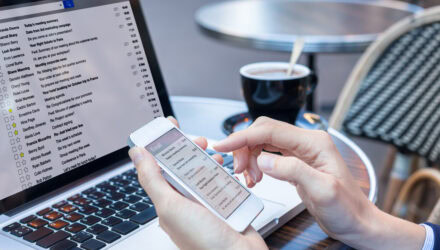 Person using smartphone and laptop for digital communication at a cafe.
