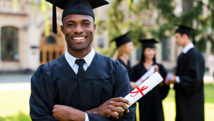 Happy graduate holding diploma at graduation ceremony outdoors.