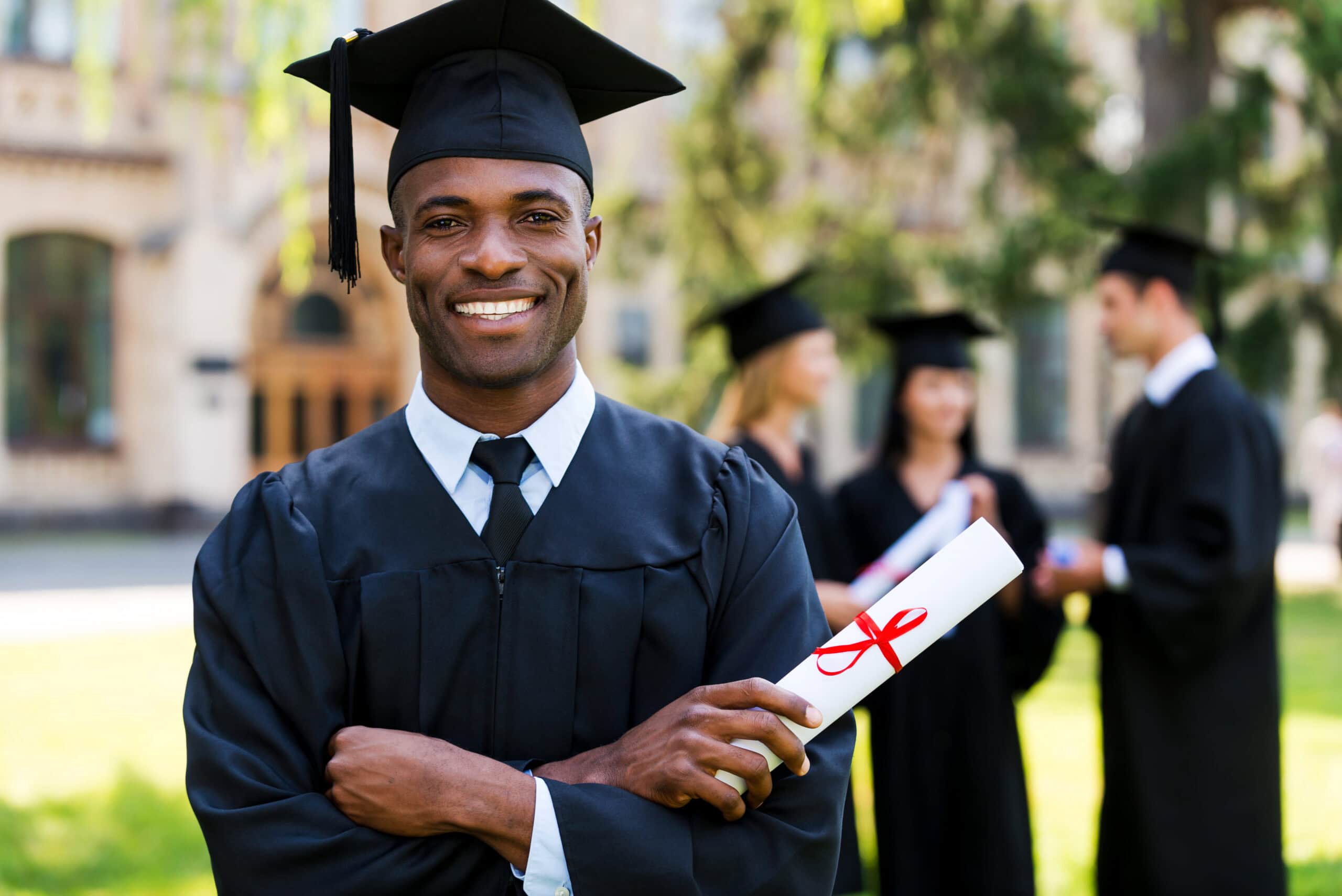 Happy graduate holding diploma at graduation ceremony outdoors.