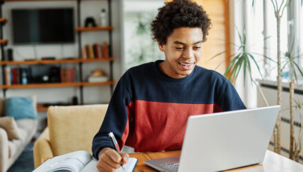 Young Woman Working on a Laptop | i3solutions Young woman working on a laptop with a notebook and pen at home.