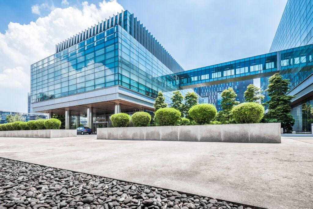 Modern glass office building with landscaped surroundings and blue sky.
