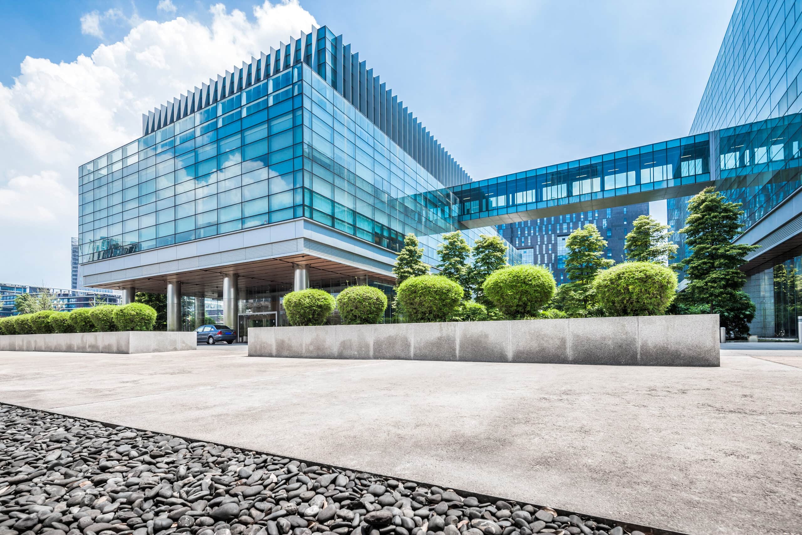 Modern glass office building with landscaped surroundings and blue sky.