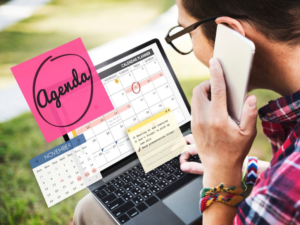 Person using laptop and phone with calendar and agenda notes for productivity.