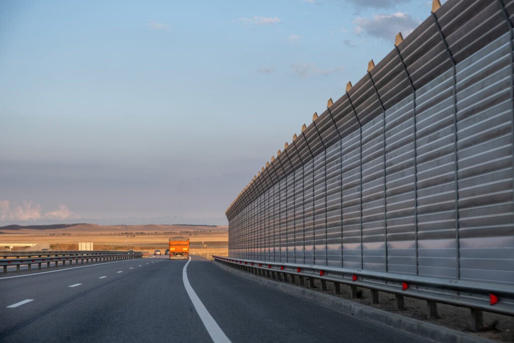 Highway with sound barrier wall and truck driving away in the distance.