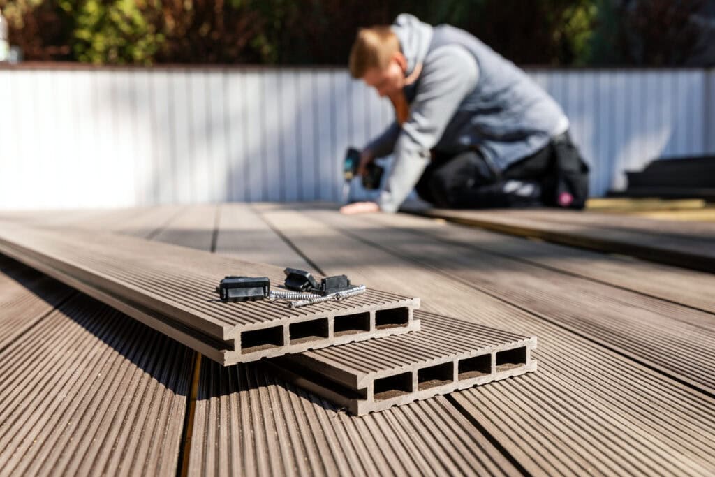 Man installing composite decking boards outdoors with tools.