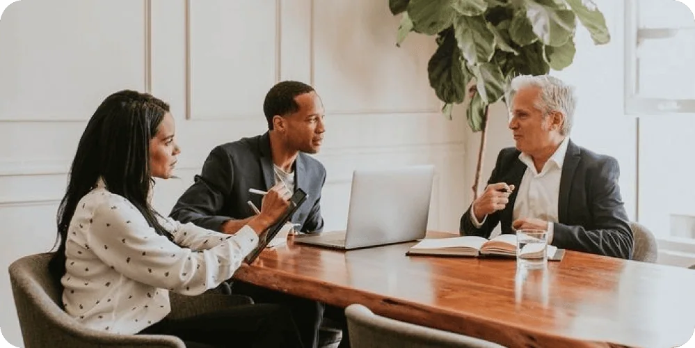 Built for Control and Accountability | i3solutions Business meeting with diverse professionals discussing AI services at a wooden table.