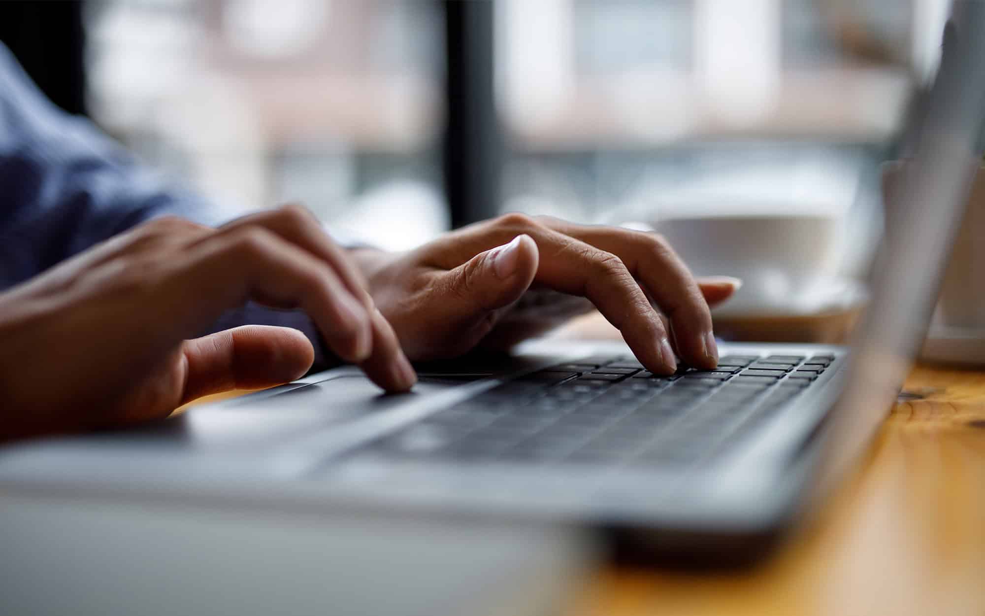 Close-up of hands typing on computer keyboard panoramic banner | i3solutions Person typing on a laptop keyboard for technology and business work.